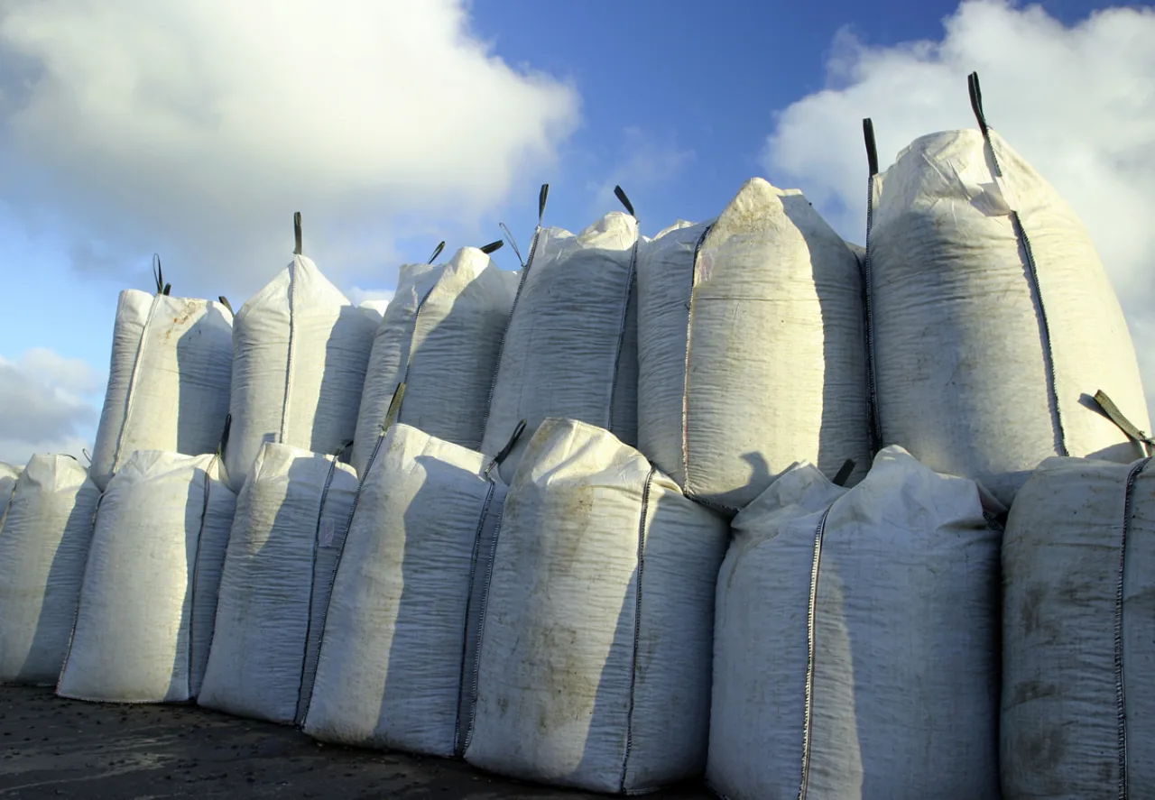 White bulk bags stacked outdoors under a blue sky.